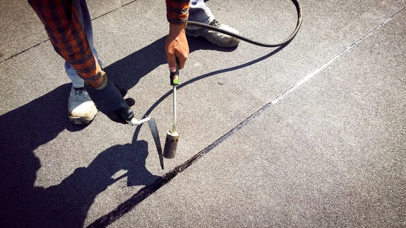 Roofer sealing a failed joint on a London flat roof during a repair