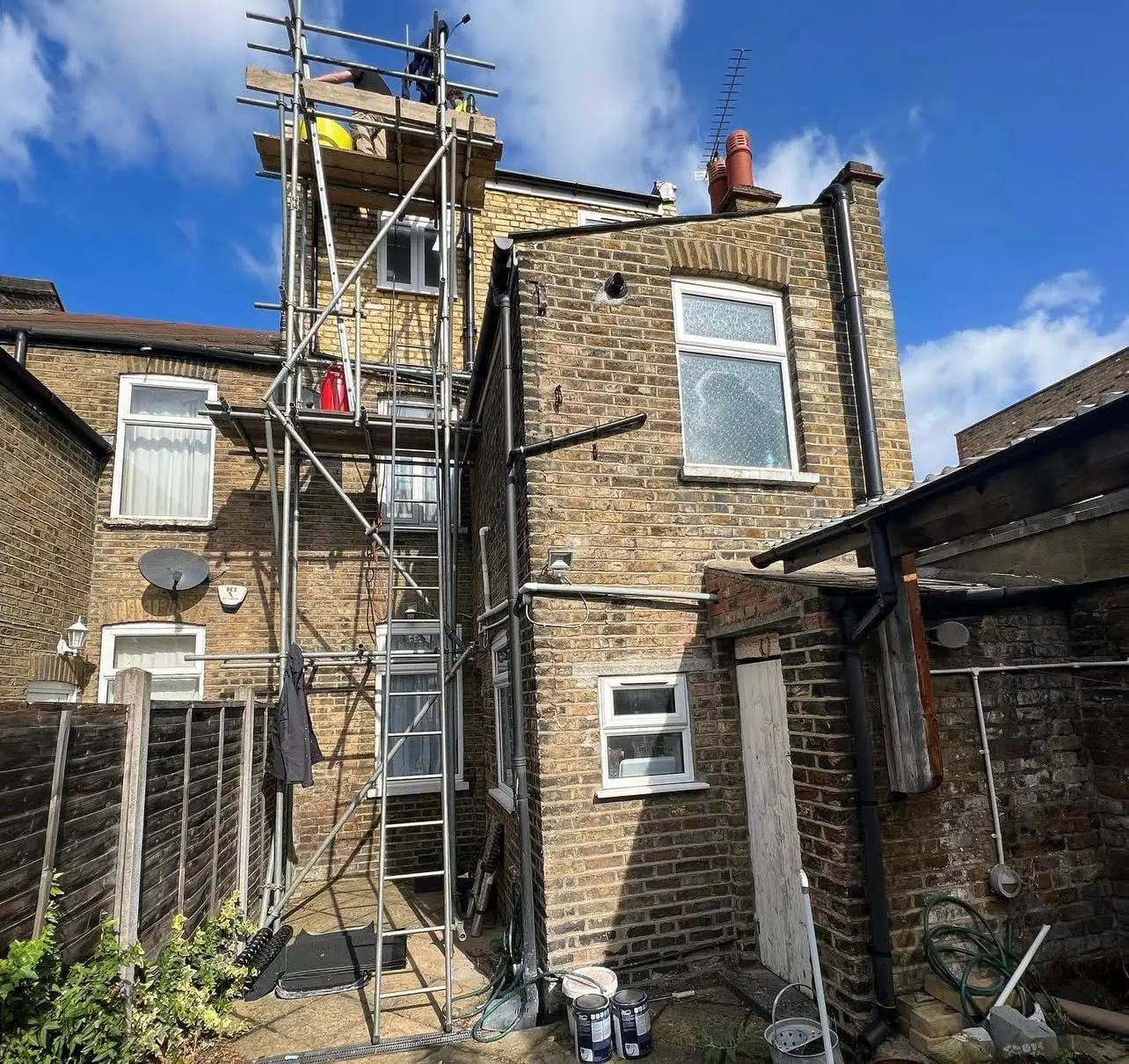 Scaffolded rear elevation of a London property with a roofer working at high level