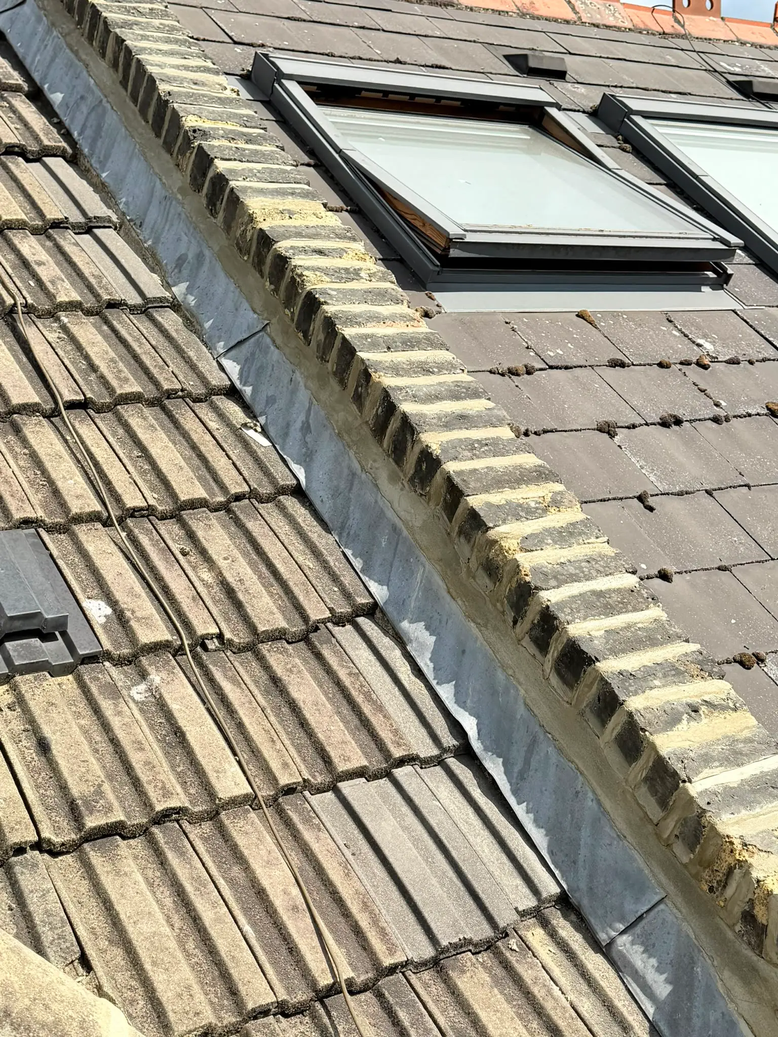 Repointed brick abutment beside a roof window and tiled roof valley in London